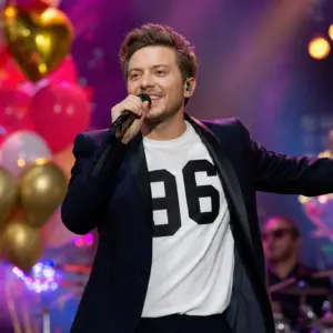 Fotorealistyczna scena urodzinowej imprezy i występu młodego polskiego wokalisty w odświętnym stroju oraz koszulce z numerem 96